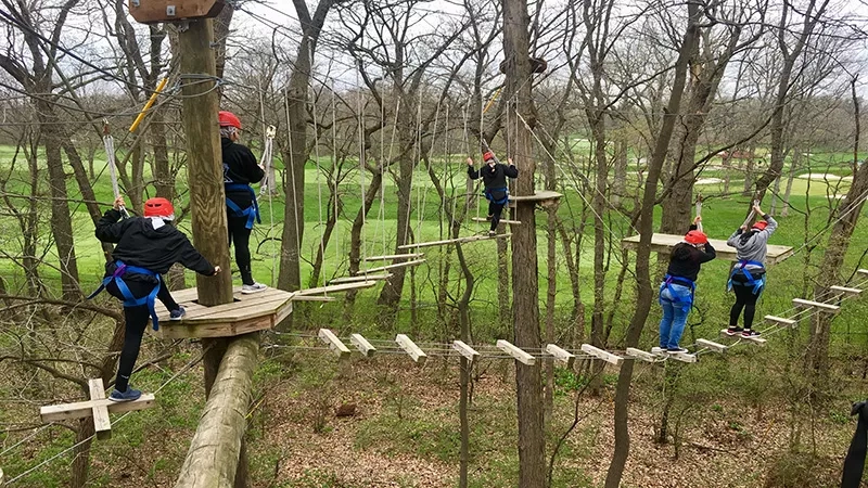 A group of people are on a rope course with a golf course in the background.
