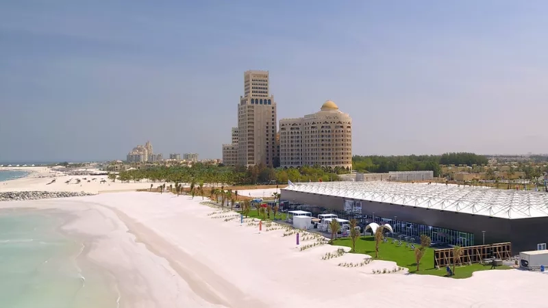 A scenic view of the beach with the Al Hamra International Exhibition & Conference Centre in the distance.
