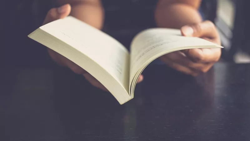 Close-up of hands holding an open book with a black table in the background.