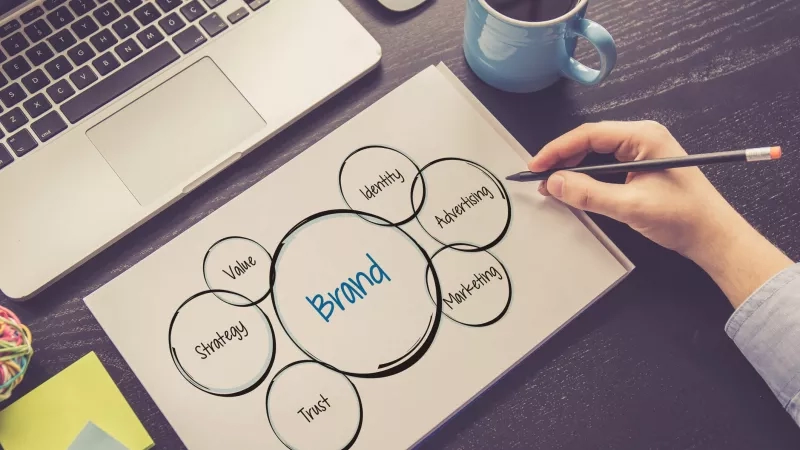Person mapping out hotel branding strategy on paper with laptop and coffee.