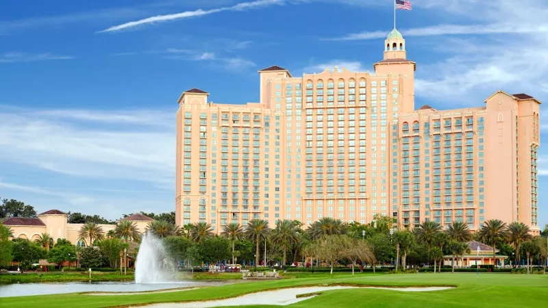 Exterior of Orlando resort with golf course, palm trees, fountain, and blue sky with clouds.