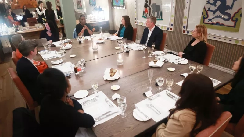 Group of people sitting around a table in a restaurant, with wine glasses and food on the table.