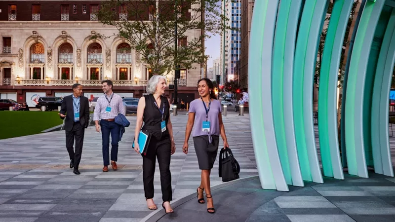 Four people walk on a striped concrete path past a green and white sculpture.