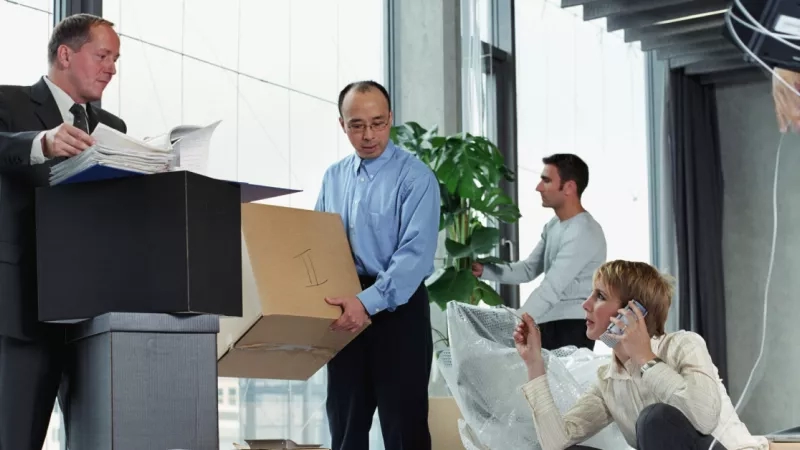A group of people are standing near a cardboard box and a woman on the phone.