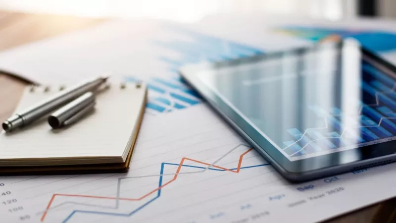 Pricing strategy data on paper and tablet with pens on a table in an office.