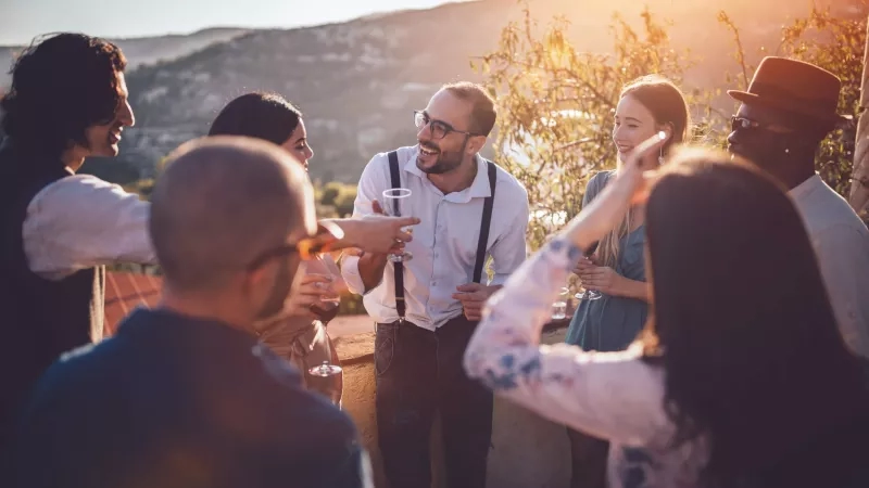 Group of people drinking wine at winery event with mountain view and warm sunset ambiance.