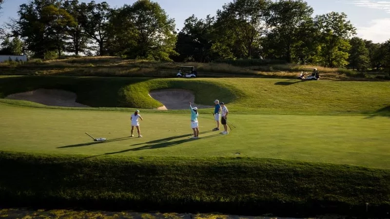 Three golfers on a golf course, with two golf carts in the background at the Farm House Inn.