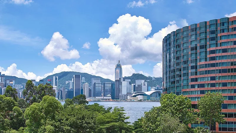The InterContinental Hong Kong, surrounded by trees and overlooking Victoria Harbour, with a cityscape in the background.