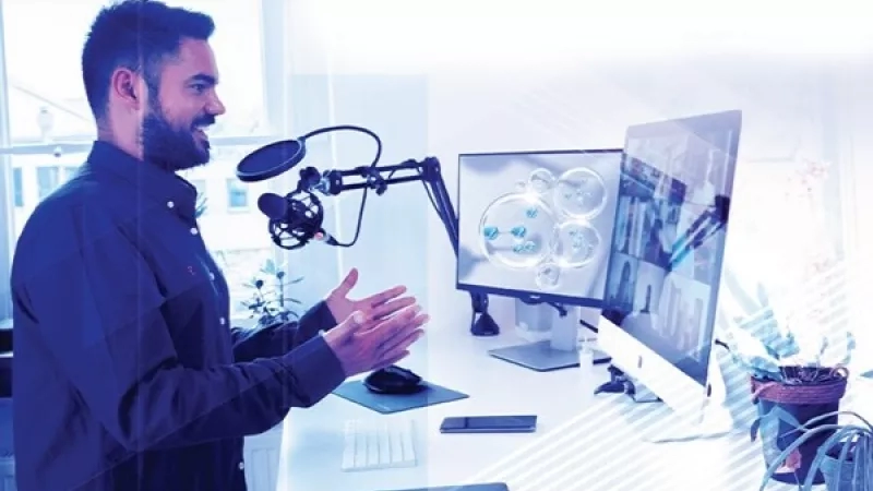 Man standing in front of desk with mic, monitors, and keyboard, with potted plants adding ambiance.