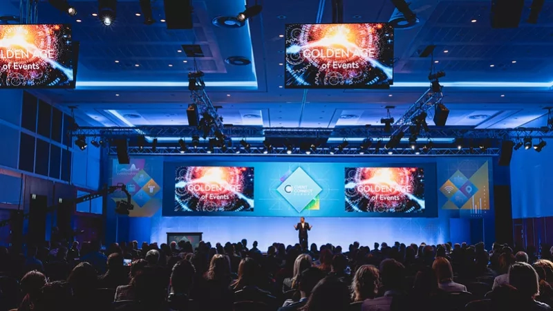 A man is giving a presentation at a conference with a crowd of people watching him.