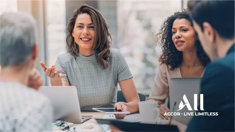 Three women and one man are sitting at a table with laptops, smiling, and the words "Accor Live Limitless".