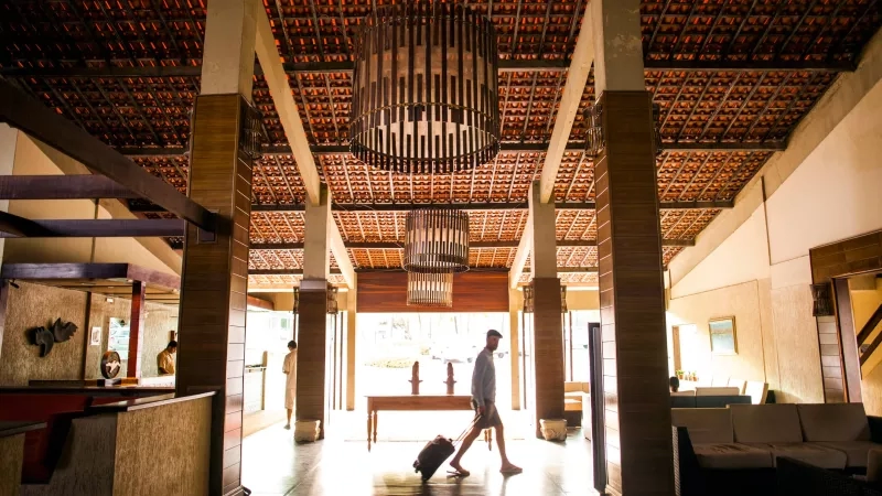 Man walking through the lobby of a hotel with large chandeliers hanging from the ceiling.