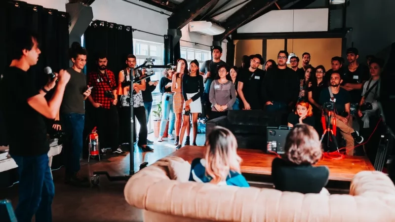 People networking at an event with a speaker and audience in a room with a wooden table and couch.