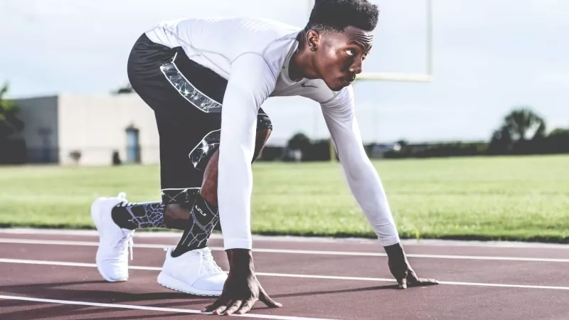 A male athlete is seen in the image preparing to start a race on a track.