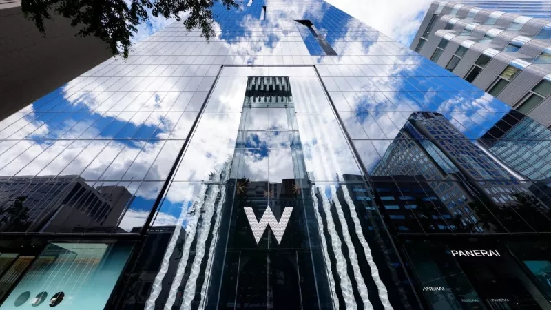 The large glass building reflects the clouds and other buildings in the area.