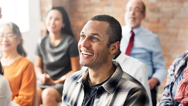 Attendees at a support group meeting are smiling and laughing while sitting in a circle.