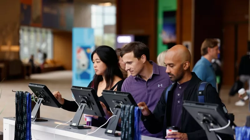 Three people looking at computer monitors with lanyards hanging from the monitors at a convention center.