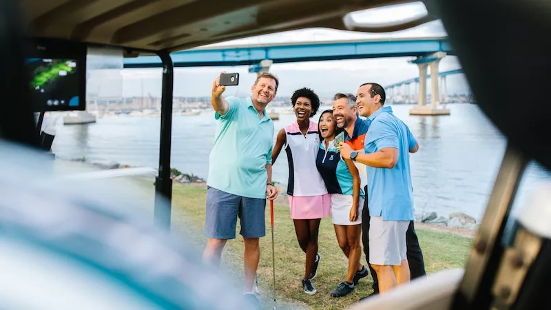 A group of friends taking a selfie at the Coronado Golf Course with a body of water in the background.