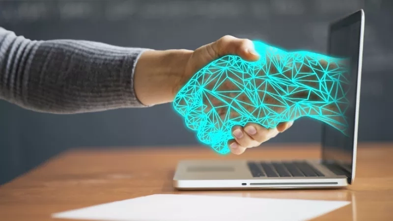 Two hands shaking with a glowing handshake graphic and a laptop in the background.