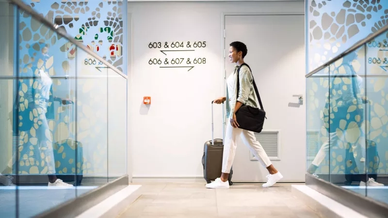 A bleisure traveler at a hotel, walking with luggage, with modern decor and natural light.