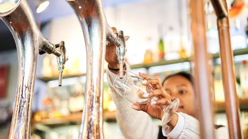 A woman is pouring a glass of beer from a beer tap at a brewery.