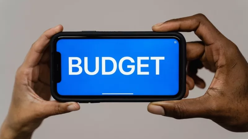 A person holding a phone with a blue screen that says budget in white letters.