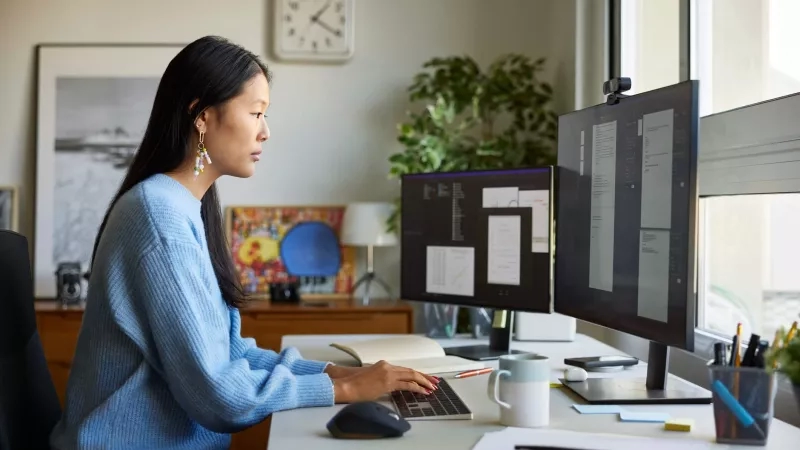 Woman on a computer with many documents in front of her and a large window.