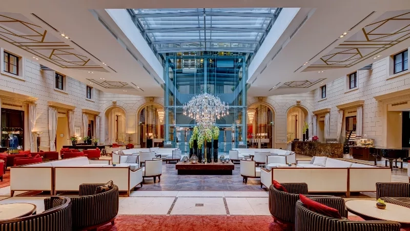 The Kempinski Vienna Hotel lobby features a large glass atrium, a grand chandelier, and luxurious furnishings.