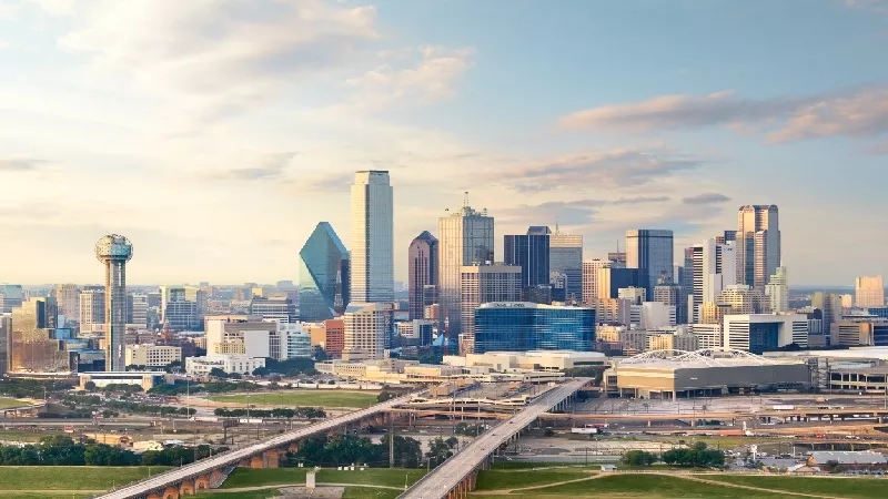 A view of the Dallas skyline with tall buildings, a bridge, and a cloudy sky.