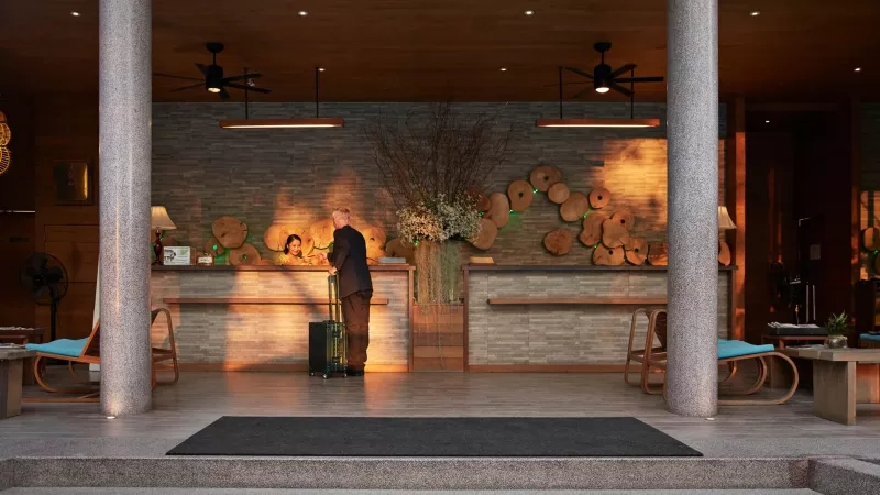 Hotel entrance with wood decor and guest speaking with staff at the reception desk.