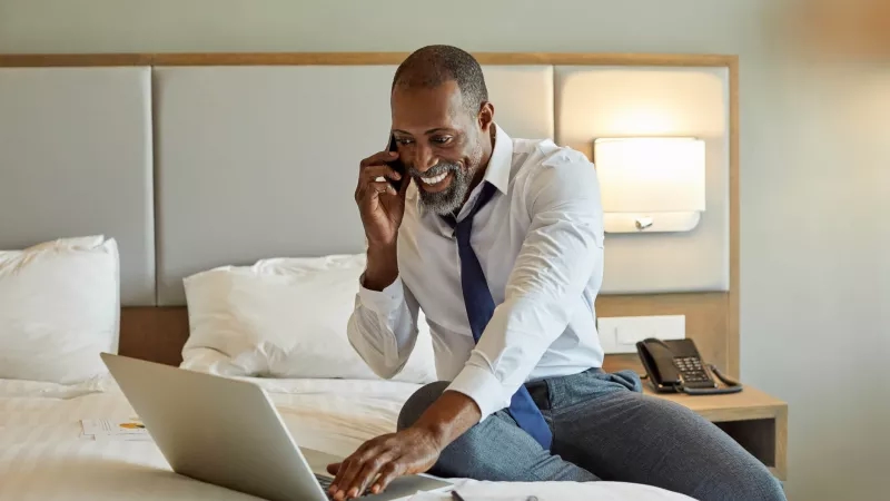 Man working on laptop while talking on phone in hotel room at Element San Jose Airport.