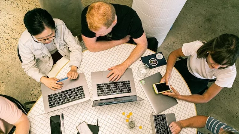 A group of people are working on laptops, a glass of water, and a cup of coffee on a table.