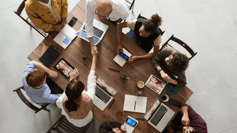 An aerial view of a group of people having a meeting around a table with laptops and cellphones.