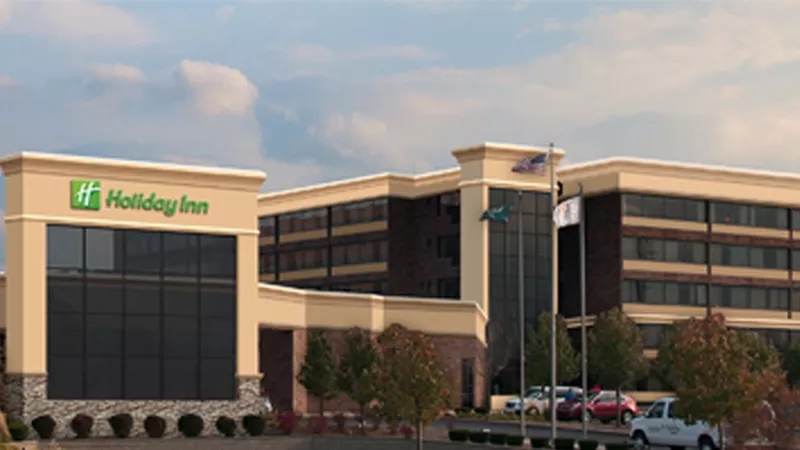 Holiday Inn exterior building with a sky background, cars, trees, and flagpoles in front of the building.