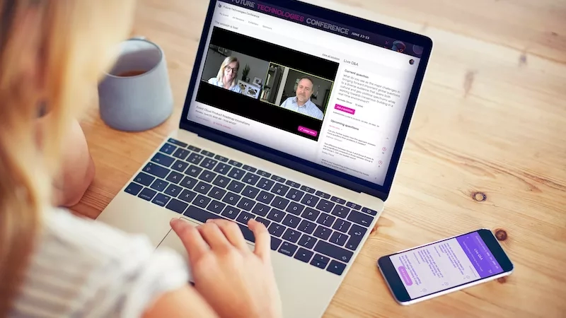 A woman typing on her laptop with a virtual mockup of a conference on her screen.