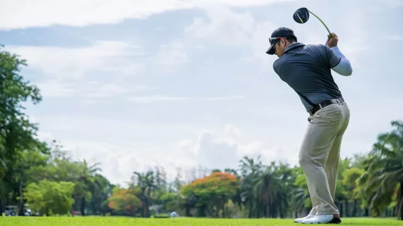 A golfer is hitting a golf ball with a club on a lush green golf course.