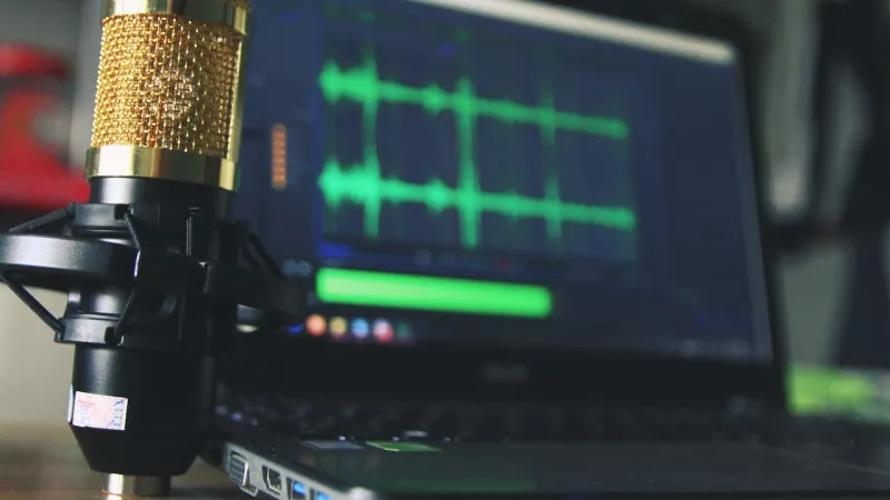 A microphone on a laptop computer with an audio editing program open on the screen.