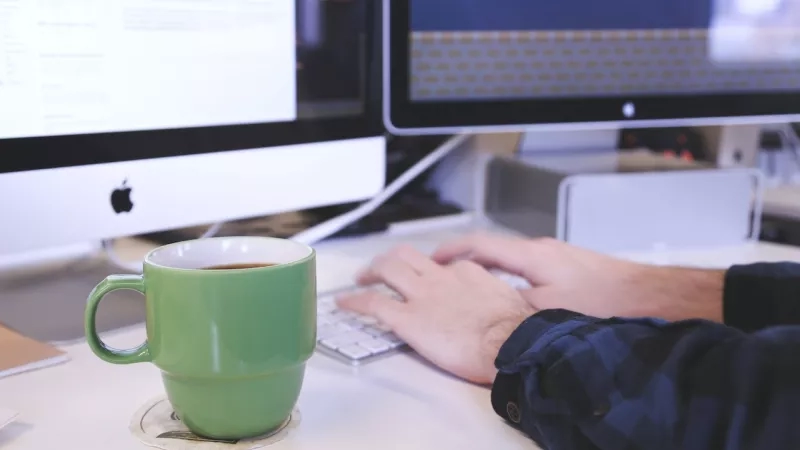 A man typing on a keyboard with a green mug on the table.