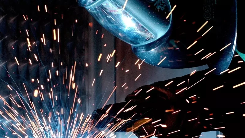 Worker wearing welding mask and gloves and welding machine with sparks and bright light in a workshop.
