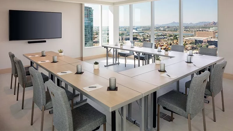 Conference room with chairs and tables, flat-screen TV, and large windows offering city views.