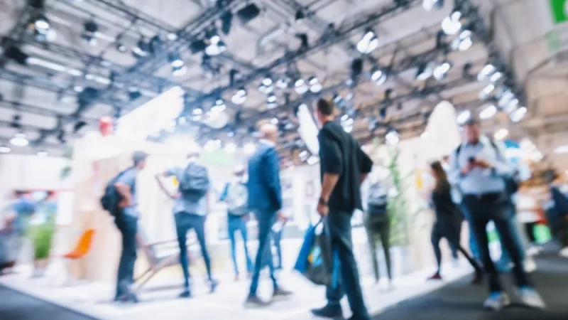 A group of people are roaming around an event with a blurred background and a spotlight above them.
