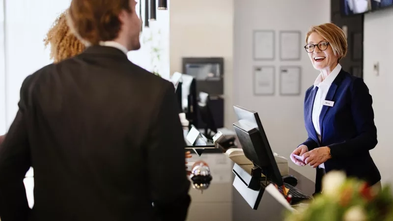 Receptionist Nina at the front desk of the hotel, greeting a guest with a smile.