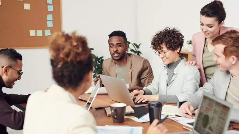 A group of coworkers are gathered around a table and working together on a project.