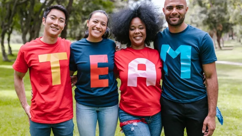 Four people wearing T-shirts that spell out the word 'team' stand together in a park.