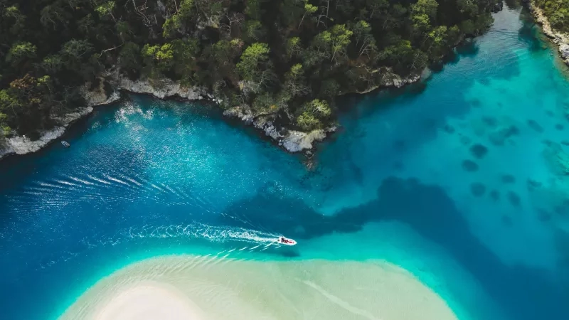 Tropical destination with a boat on blue water, surrounded by lush greenery, and white sandy beach.