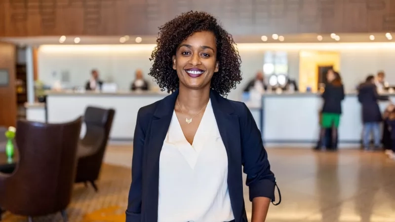 Woman in front of a hotel desk, smiling and wearing a navy blazer and white blouse.