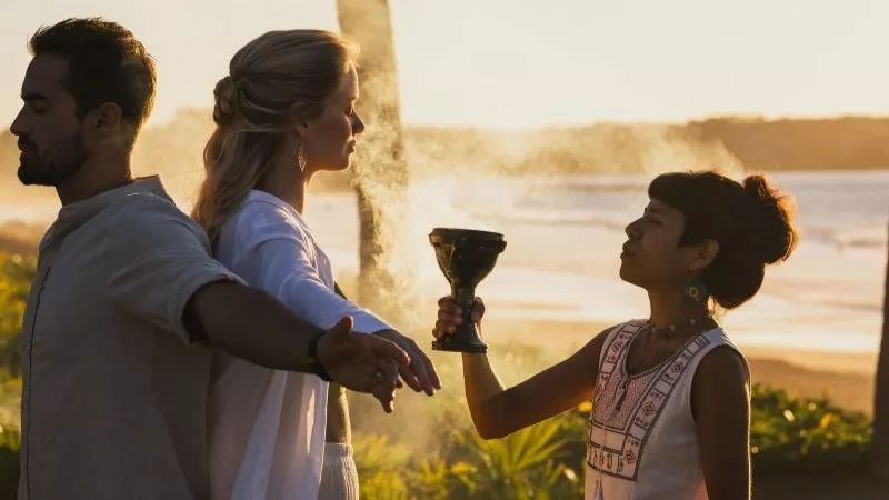 Three people at Conrad Punta Mita, Mexico, standing in front of a beach, performing a traditional ceremony.
