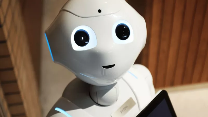 A white robot with large eyes is holding a tablet with the word Pepper written on it.