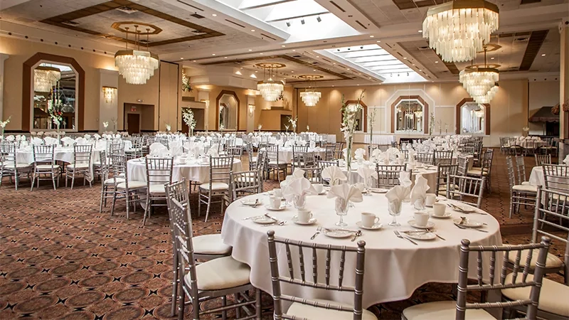 A large banquet hall with round tables, white tablecloths, and crystal chandeliers.