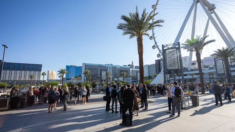 People gather at the Caesars Forum in Las Vegas, with buildings and palm trees in the background.